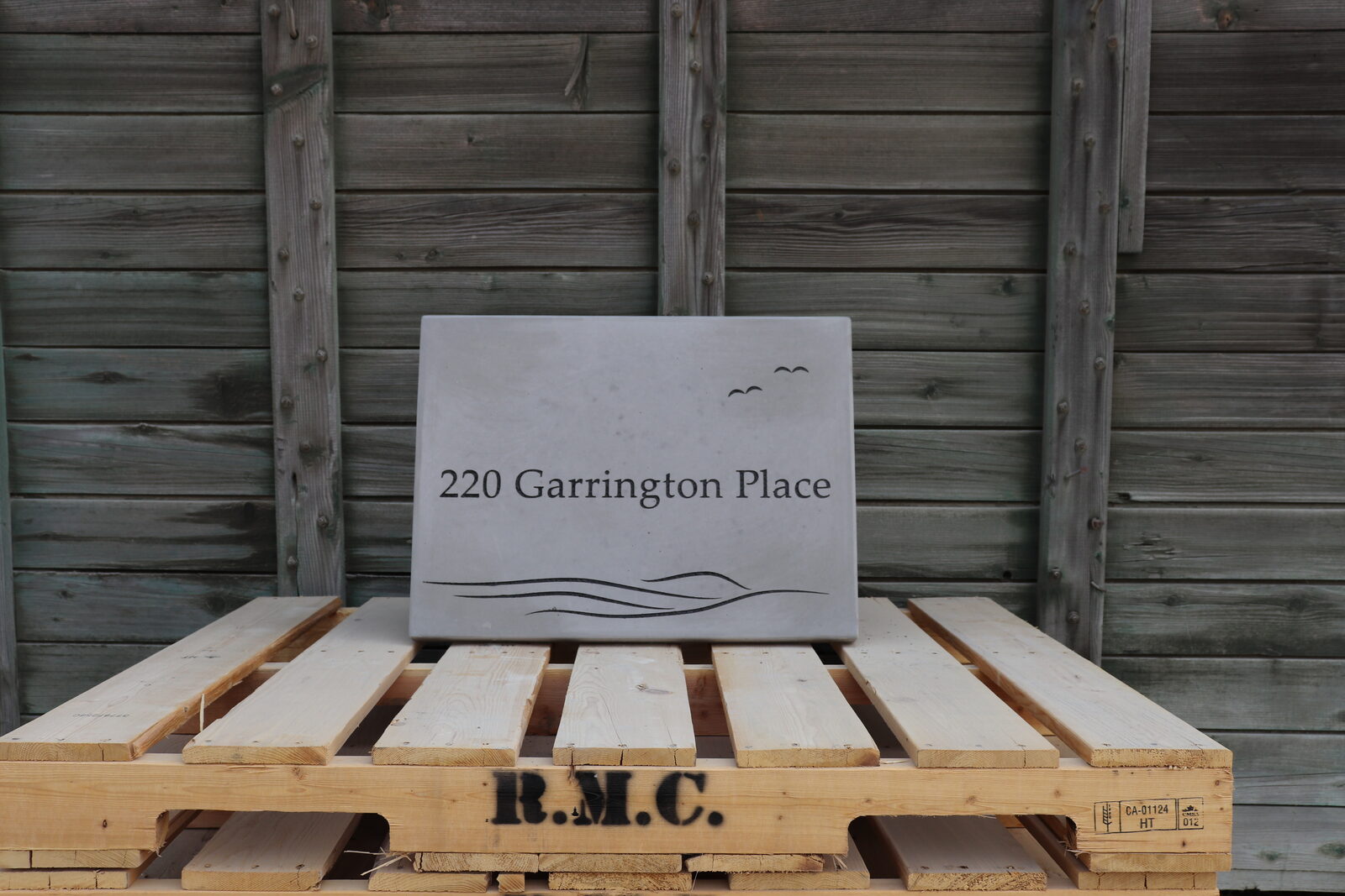 Engraved concrete address plaque in dark grey with gulls and flowing water lines beneath the address