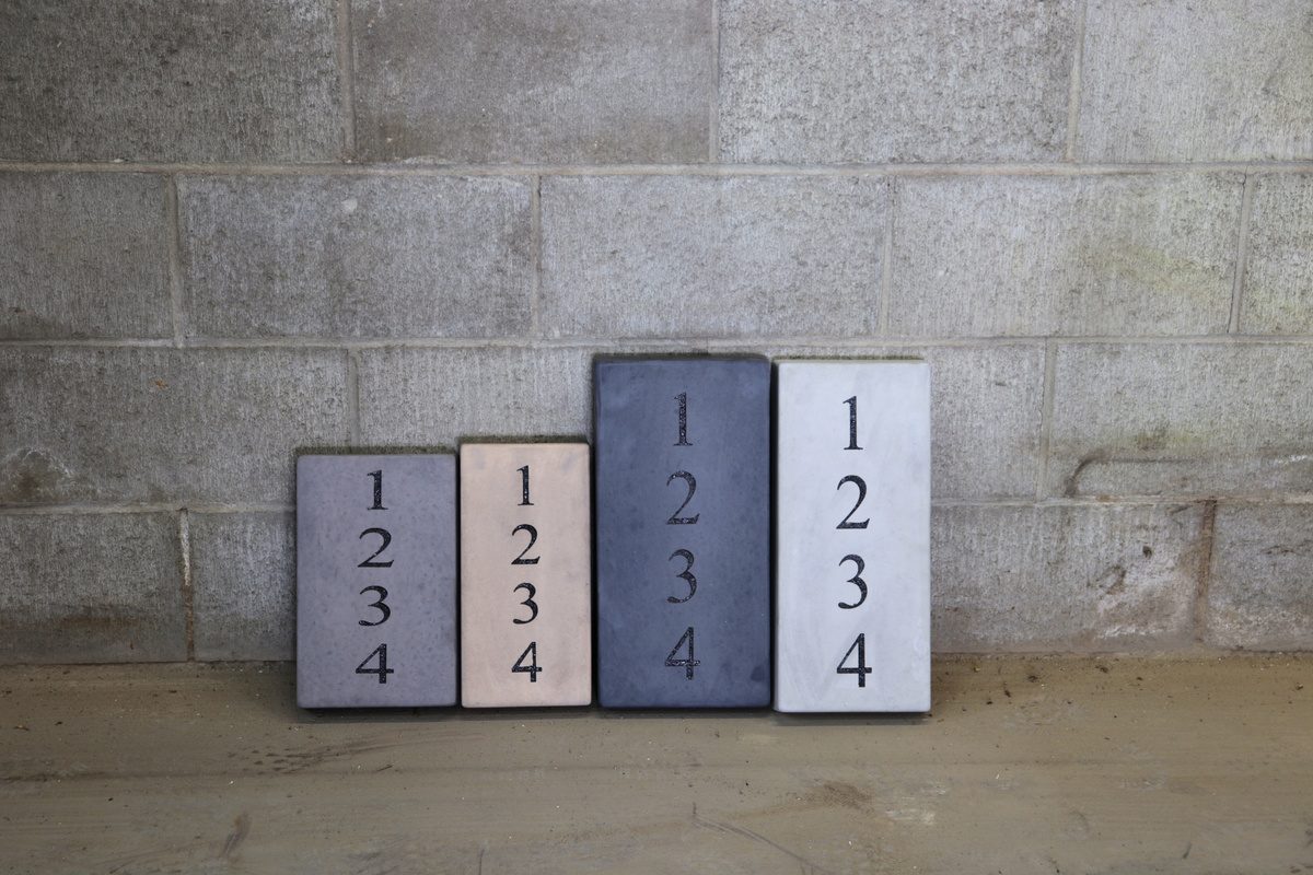 Four Rocky Mountain Concrete engraved address plaques in different colours, lined up against a block wall